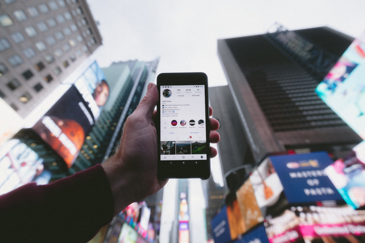Mann hält Smartphone vor die Gebäude des Time Square, Hochhäuser, Neon-Werbung